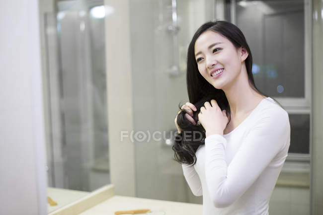 Chinese woman combing hair in bathroom — Stock Photo