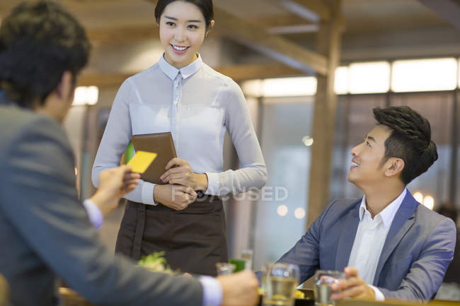 Empresarios chinos pagando con tarjeta de crédito en restaurante - foto de stock