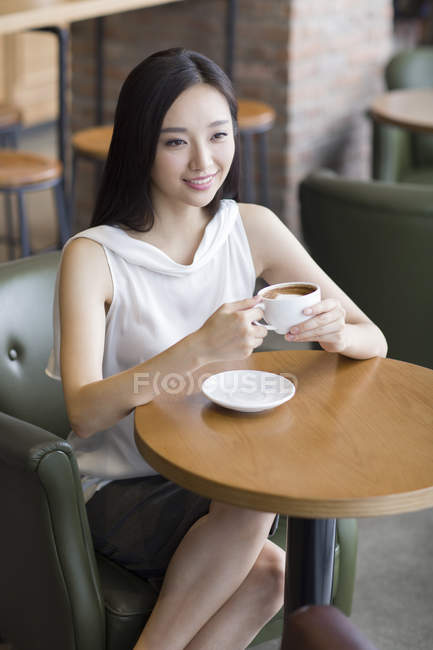 Jovem chinesa segurando xícara de café no café — Fotografia de Stock