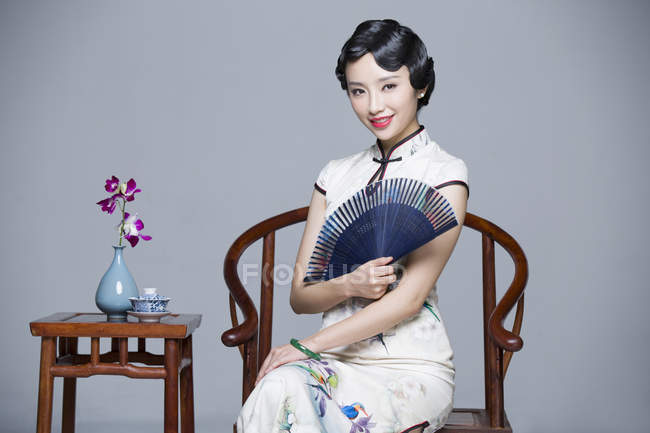 Chinese woman in traditional dress sitting at tea table and holding handheld fan — Stock Photo