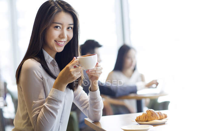 Mujer china posando con taza de café en la cafetería - foto de stock