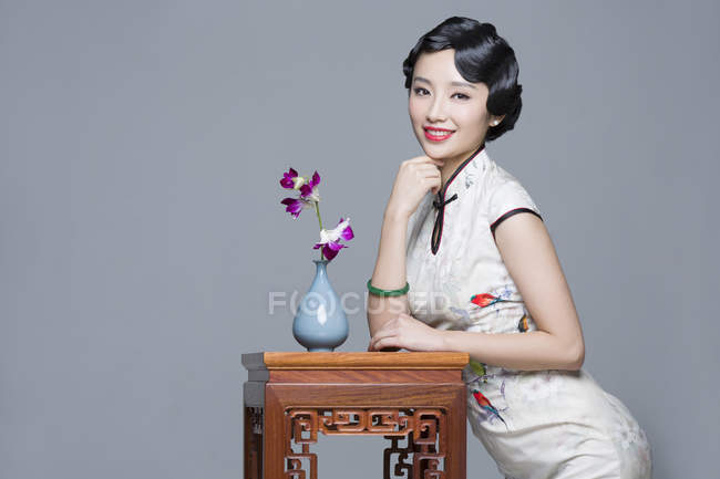 Китайська жінка в традиційному одязі, спираючись на стіл з орхідей — стокове фото