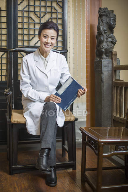 Femmina medico cinese seduto sulla sedia e tenendo diario — Foto stock