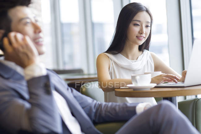 Chinese woman working with laptop with man talking on phone in foreground — Stock Photo