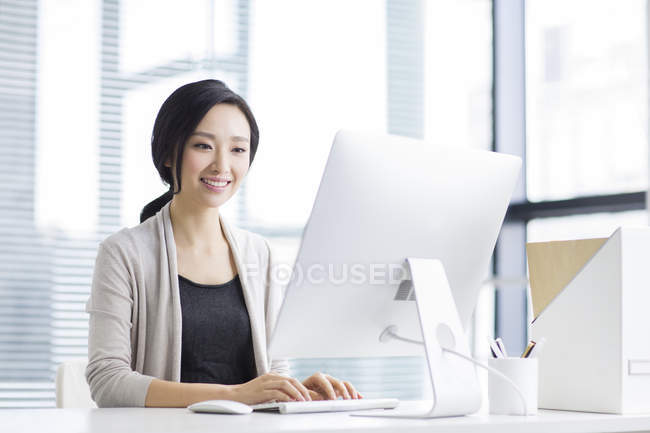 Китаянка, работающая с компьютером в офисе — стоковое фото