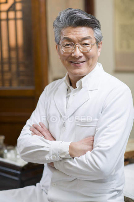 Médico chino senior de pie con los brazos cruzados - foto de stock