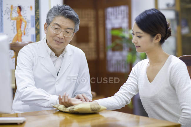 Senior médico chino tomando pulso de paciente femenino - foto de stock