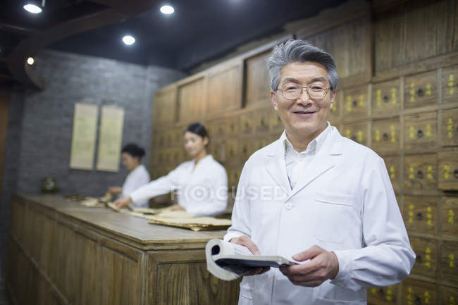 Chinese senior man holding book in traditional pharmacy — Stock Photo