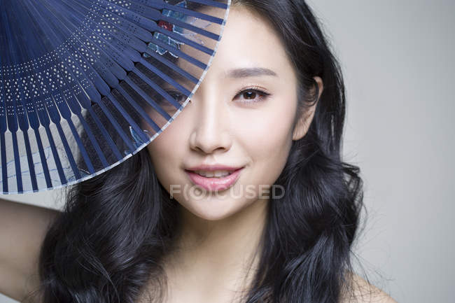 Chinese woman covering face with folding fan — Stock Photo