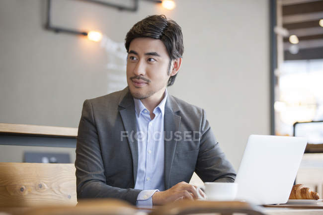 Chinese businessman sitting with laptop in cafe — Stock Photo