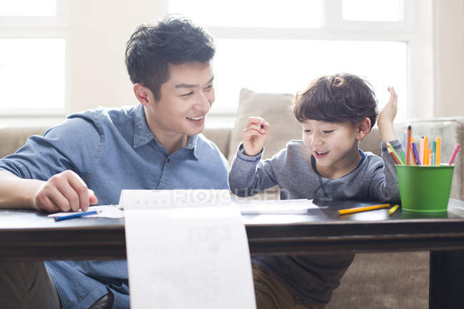Chinese father and son doing homework together at table — Stock Photo