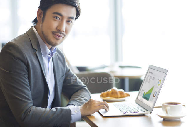 Homme d'affaires chinois assis avec ordinateur portable dans un café — Photo de stock