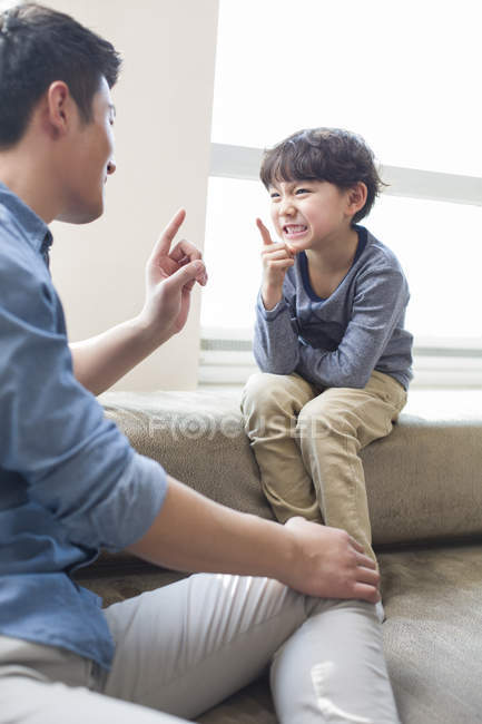 Chinese father and son sitting on sofa and funny gesturing — Stock Photo