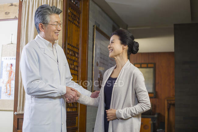 Médico chino estrechando la mano con la mujer madura - foto de stock