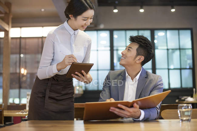 Chinese man ordering in restaurant with waitress — Stock Photo