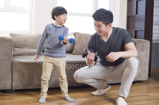 Chinese father and son exercising with dumbbells at home — Stock Photo