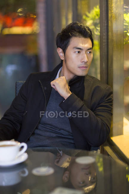 Pensive Chinese man sitting at street cafe — Stock Photo