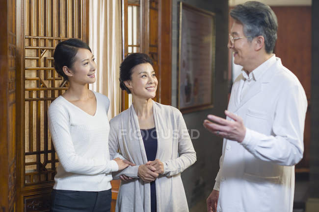 Médico chino mayor hablando con pacientes en el pasillo - foto de stock