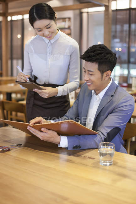 Китаец заказывает столик в ресторане с официанткой — стоковое фото