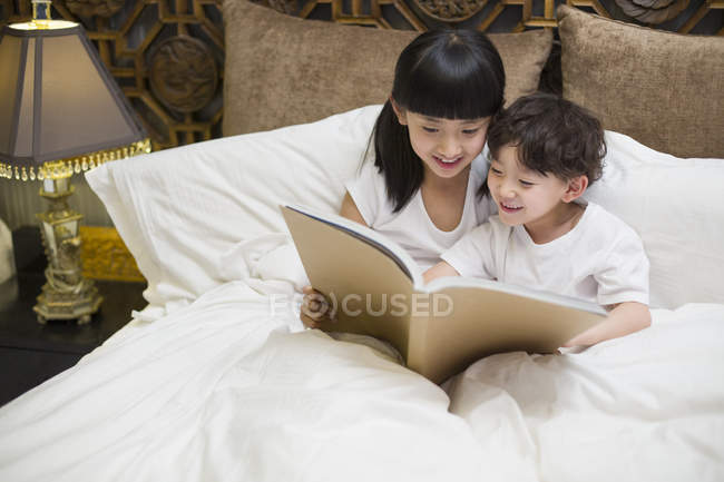 Niños chinos leyendo libro en el dormitorio - foto de stock