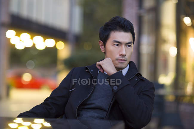 Chinese man sitting at cafe table and looking away — Stock Photo
