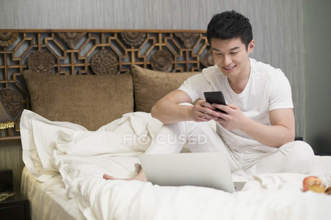 Homem chinês usando smartphone na cama — Fotografia de Stock