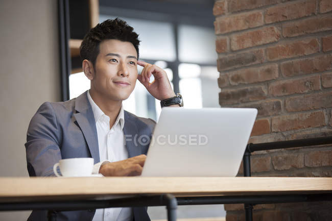 Hombre de negocios chino sentado con el ordenador portátil en la cafetería - foto de stock