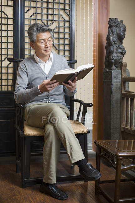 Homem chinês sênior sentado na cadeira e livro de leitura — Fotografia de Stock