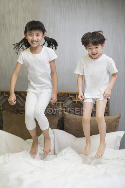 Chinese children jumping on bed — Stock Photo