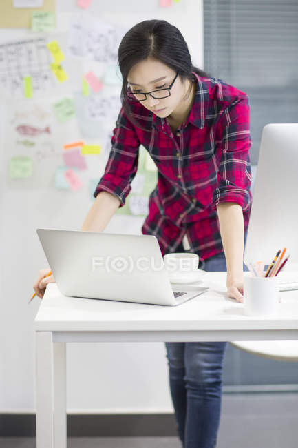 Diseñadora femenina china que trabaja con computadora portátil en la oficina - foto de stock