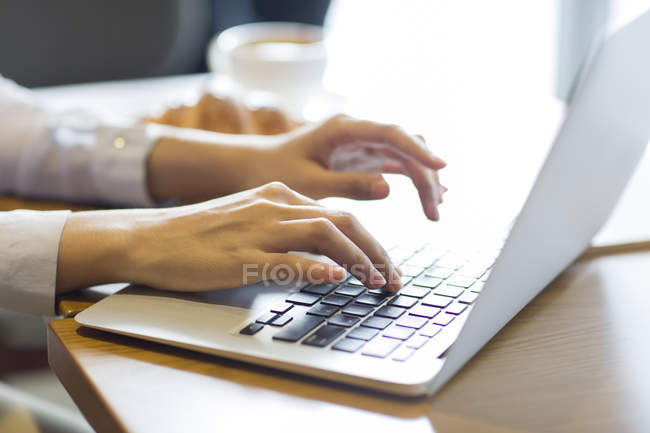 Primer plano de las manos femeninas que trabajan con el ordenador portátil en la cafetería - foto de stock