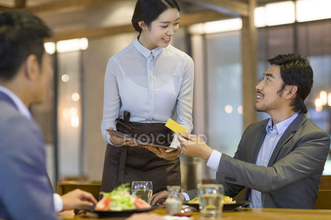 Empresarios chinos pagando con tarjeta de crédito en restaurante - foto de stock