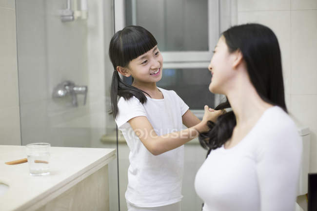 Chinese girl combing woman hair in bathroom — Stock Photo