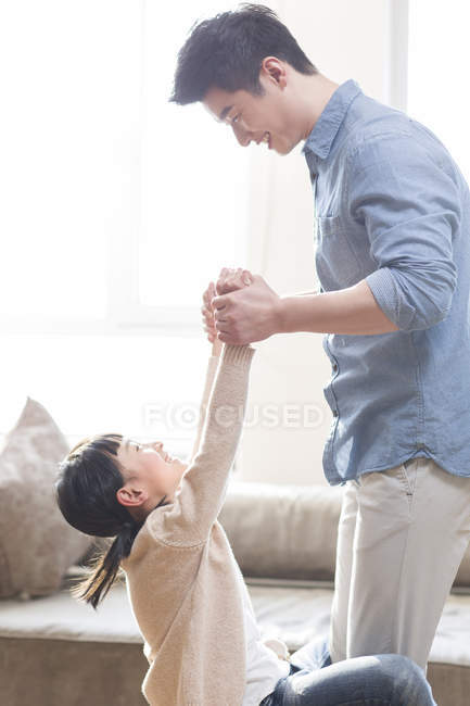 Padre e hija chinos tomados de la mano y jugando en casa - foto de stock