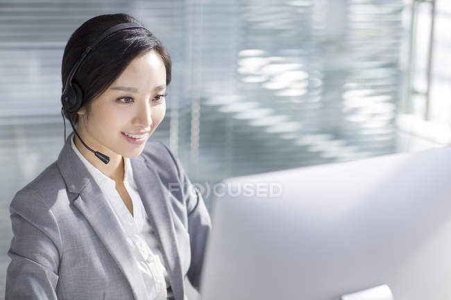 Donna d'affari cinese che utilizza auricolari sul posto di lavoro — Foto stock