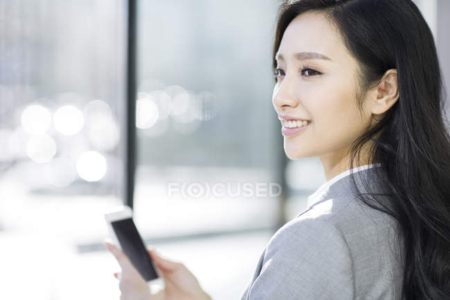 Chinese businesswoman holding smartphone and looking away — Stock Photo