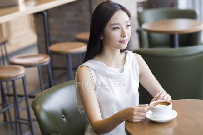 Mujer china sentada con taza de café en la cafetería - foto de stock