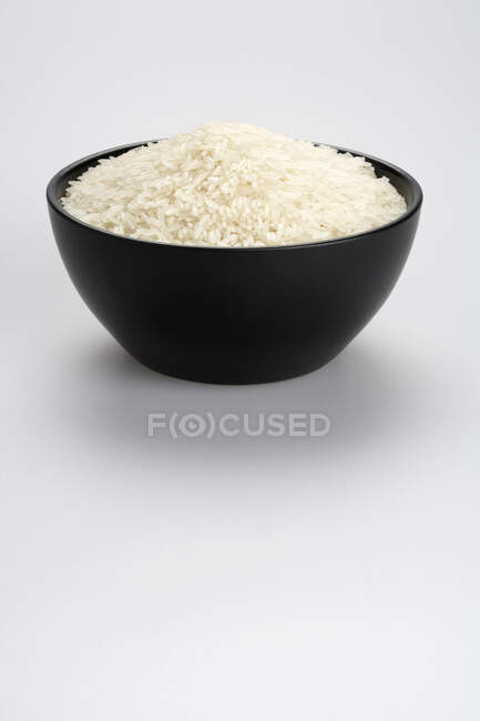 Arroz não cozido em tigela preta isolado em fundo branco — Fotografia de Stock