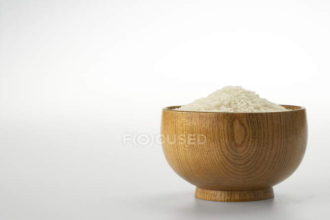 Неварений рис в дерев'яній мисці ізольований на білому тлі — стокове фото