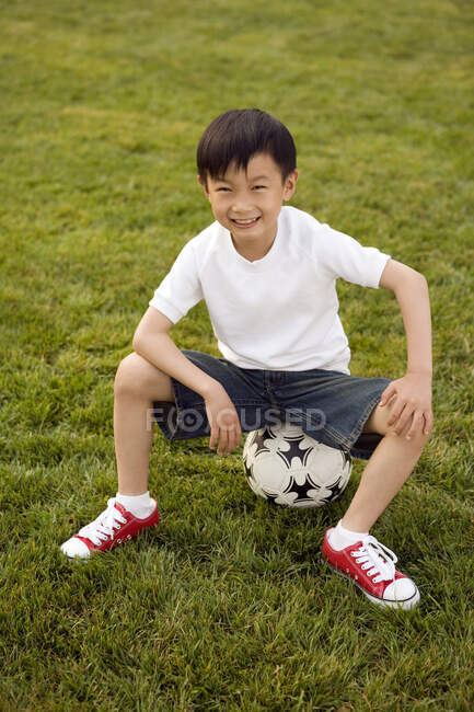 Menino chinês sentado casualmente na bola de futebol — Fotografia de Stock
