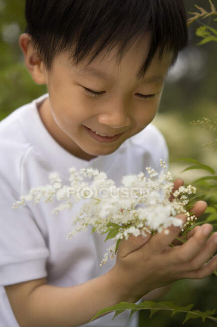 Молодой китайский мальчик, нюхающий цветы в парке — стоковое фото