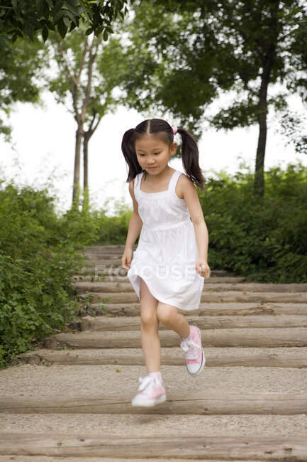 Joven china chica corriendo abajo pasos a través de parque - foto de stock