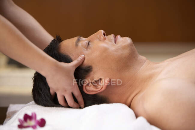 Asistente de spa dando un masaje en la cabeza a un hombre chino - foto de stock