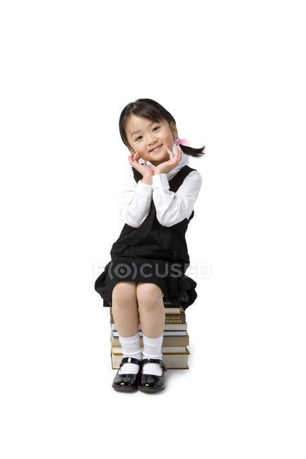 Menina chinesa senta-se em uma pilha de livros — Fotografia de Stock