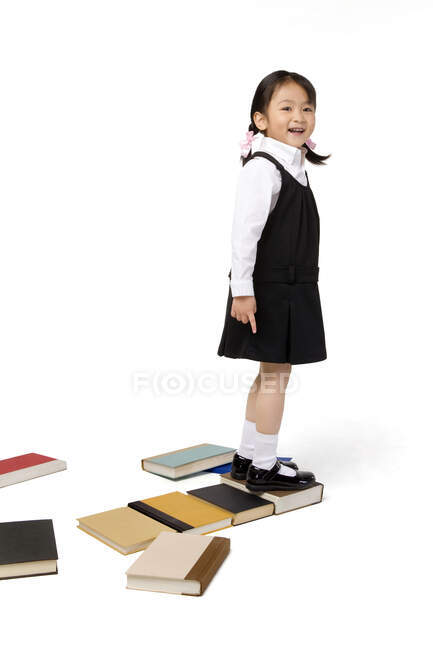 Kleines chinesisches Mädchen steht auf einigen Büchern — Stockfoto