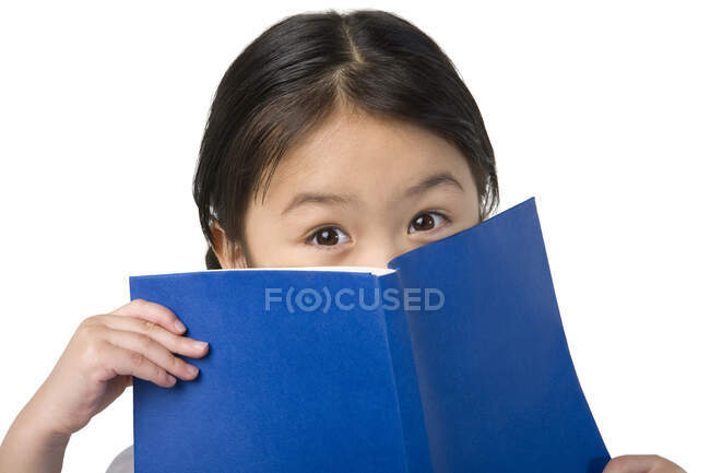 Little Chinese girl covers her face with a book — Stock Photo