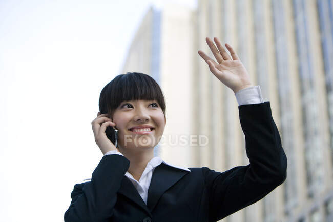 Chinese woman talking on cellphone, smiling and waving hand — Stock Photo