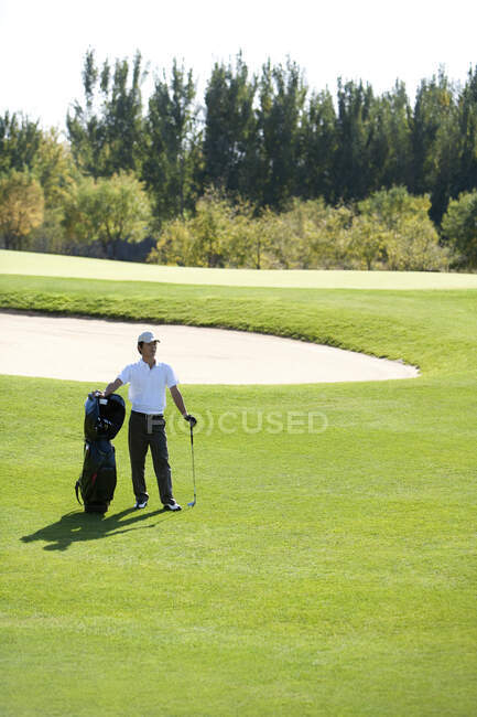 Joven hombre chino mirando el campo de golf - foto de stock