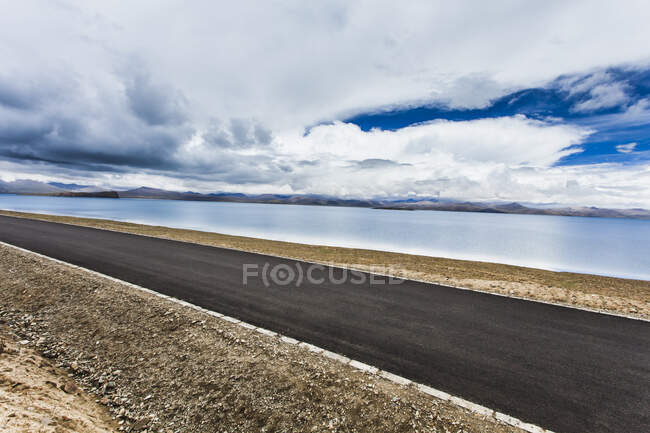 Route avec vue sur le lac et les montagnes et ciel nuageux, Tibet, Chine — Photo de stock