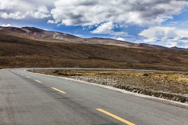 Carretera con vistas a las montañas y cielo nublado, Tíbet, China - foto de stock